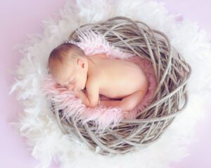 baby sleeping in a basket and a round feather surrounding the basket