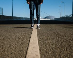 person in black pants and white sneakers standing on gray asphalt road