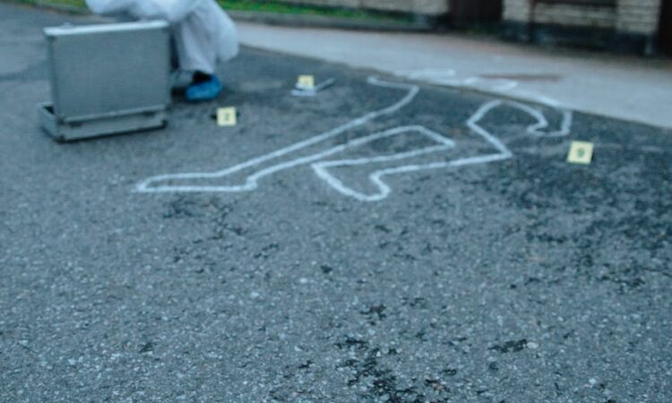 person sitting beside a chalk outline at a crime scene
