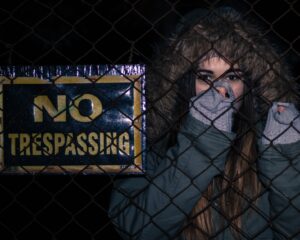 woman behind black chainlink fence with no trespassing signage