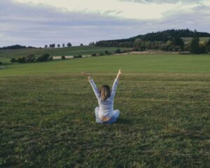 woman in gray long sleeve shirt sitting on green grass field with raised hands
