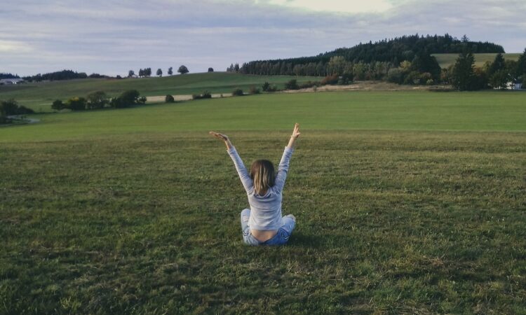woman in gray long sleeve shirt sitting on green grass field with raised hands