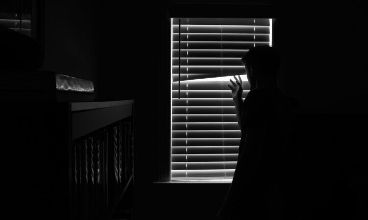 Silhouette of a person looking through window blinds in a dark room. Mystery and introspection.
