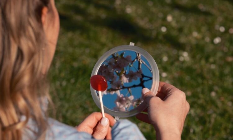 woman reflecting cherry blossoms in handheld mirror